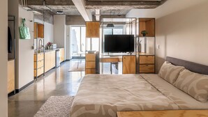 A modern bedroom with a large bed, a desk with a flat-screen TV, and a kitchenette in the background. - Triver Florencia (Mexico City)