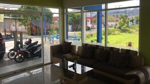 A room with a sofa and a glass coffee table, large windows with a view of the street and greenery outside. - OYO 92907 Miranda Hotel Syariah (Gresik)