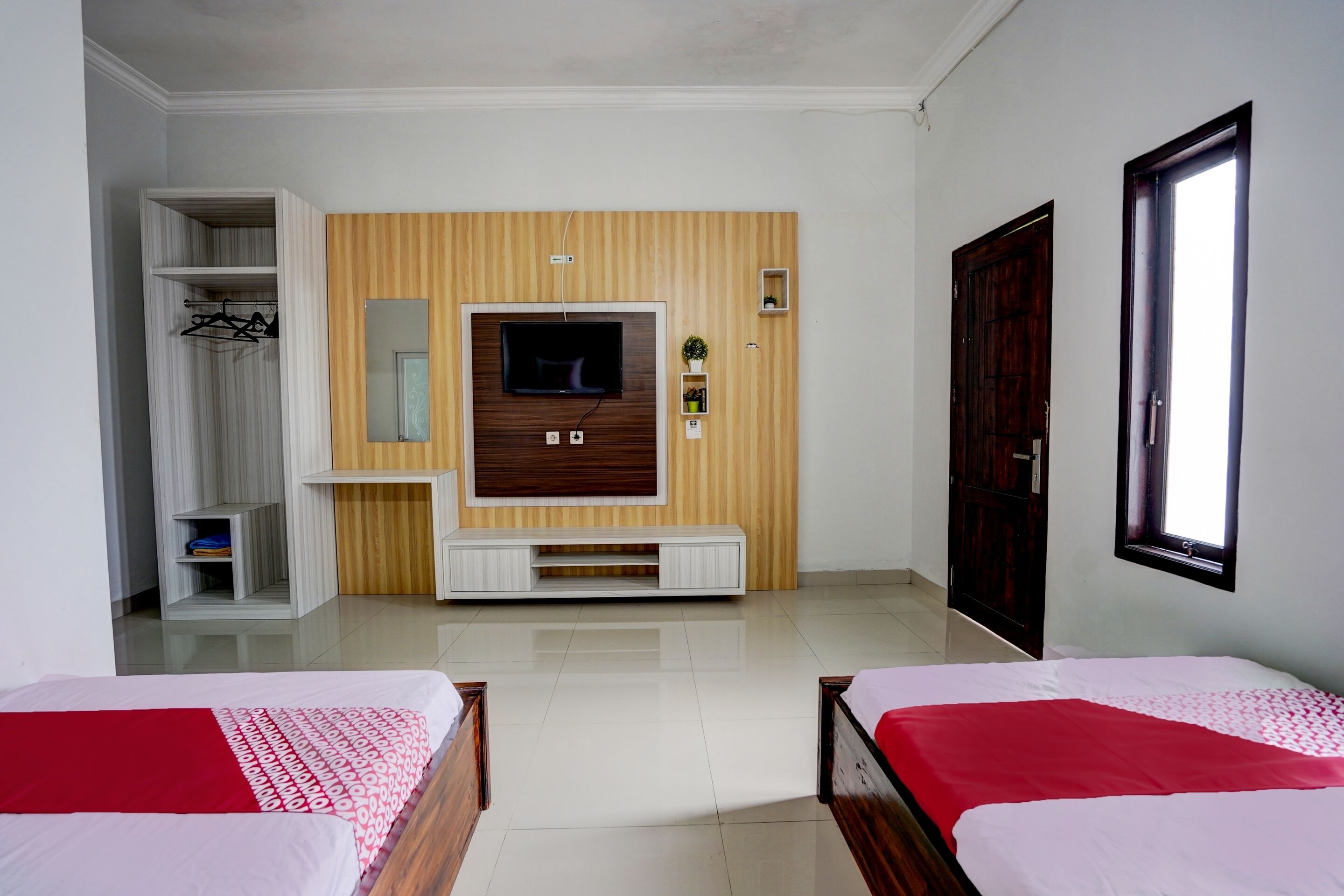 Ein Hotelzimmer mit zwei Betten, einem an einer Holzwand montierten Fernseher, einem Kleiderschrank und einem Fenster.