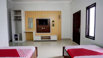 Habitación de hotel con dos camas, un televisor montado en una pared de paneles de madera, un armario y una ventana.