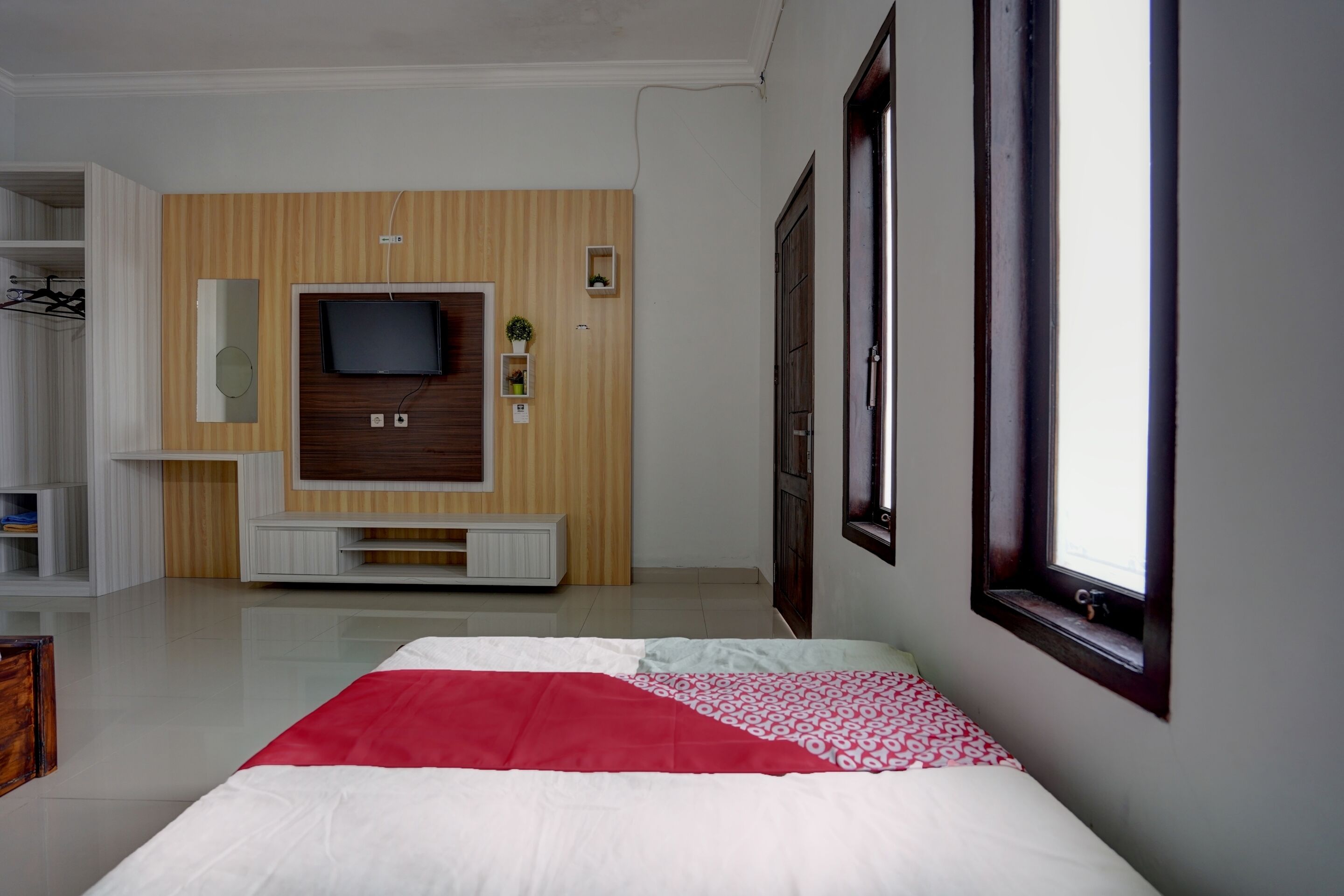 Un dormitorio con cama, televisor montado en la pared y ventana con cortinas.