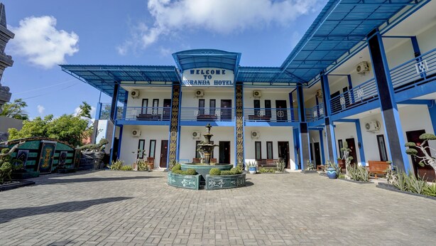 A hotel with a blue and white facade, a welcoming sign, and a central fountain. - OYO 92907 Miranda Hotel Syariah (Gresik)