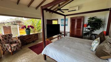 Un dormitorio con cama con dosel, televisión, escritorio y ventana con vista a la vegetación.