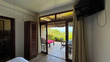 A hotel room with a bed, a TV, a wardrobe, and a sliding glass door leading to an outdoor area with a table and chairs.