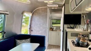Interior compacto de una caravana con comedor, kitchenette y baño pequeño.