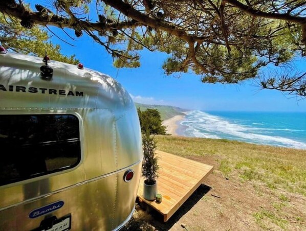 Una caravana clásica de la marca Airstream estacionada en un césped con vistas a una playa.