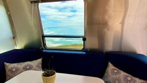 Un espacio pequeño y cerrado con ventana que da a una playa y al océano. Hay una mesa con una planta en maceta.