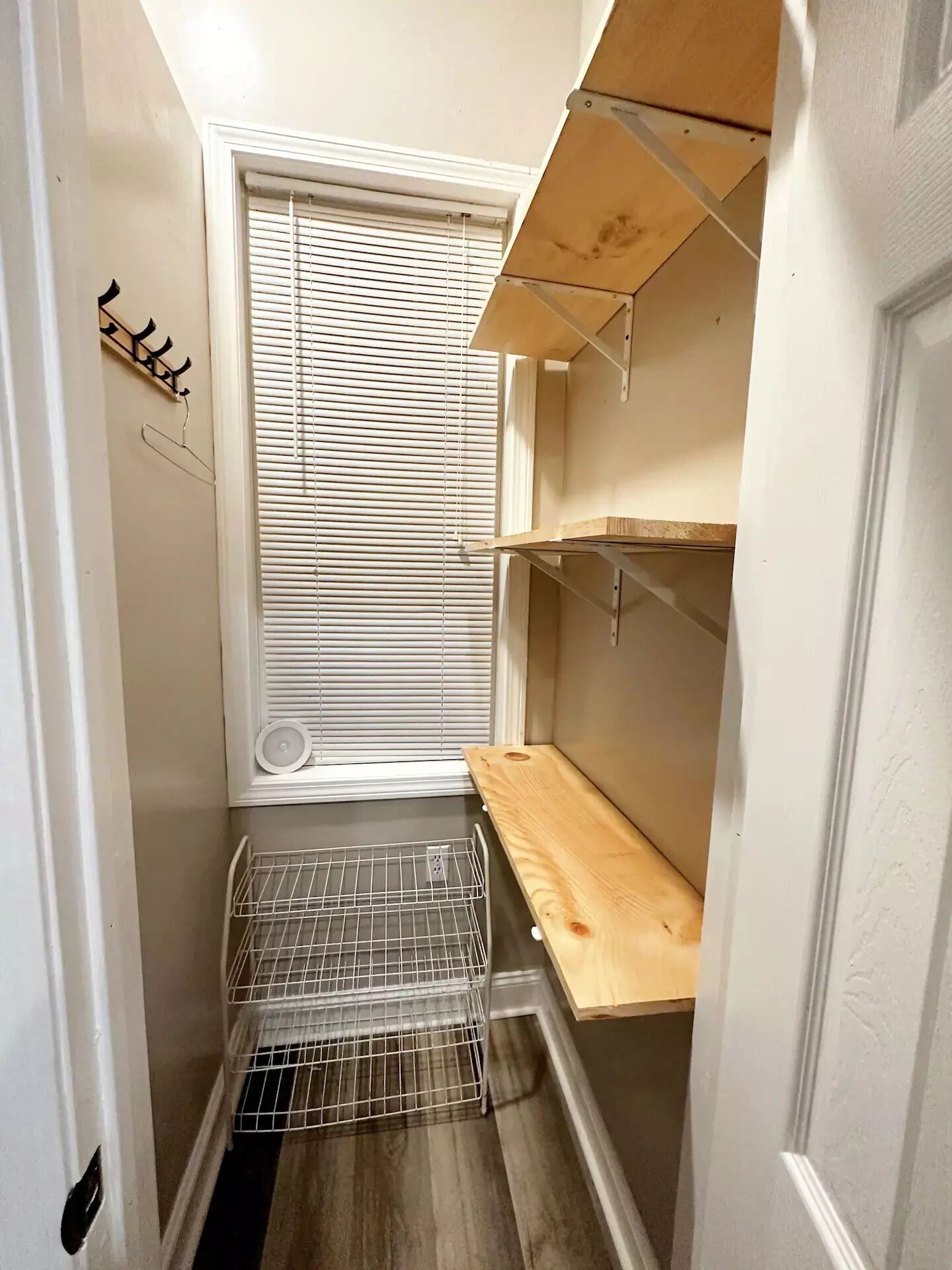 A narrow hallway with a window, a metal rack, and wooden shelves.
