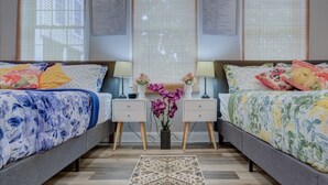 A modern bedroom with two beds, a nightstand with lamps, a decorative vase, and a patterned rug. - A Homey Haven Away from Home (Bristol)