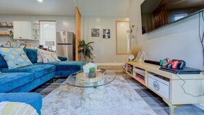 A modern living room with a blue sofa, a glass coffee table, and a white cabinet. - A Homey Haven Away from Home (Bristol)
