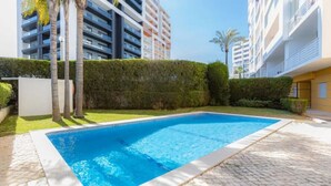 Une piscine dotée d’une terrasse dallée, entourée d’arbustes soigneusement taillés et de palmiers.