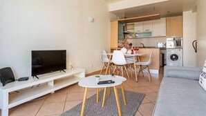 Un salon moderne doté d’un téléviseur à écran plat, d’un canapé, d’un coin repas avec des chaises et d’une cuisine équipée.