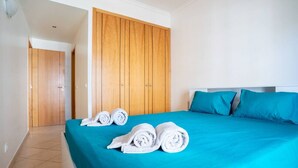 Une chambre d’hôtel avec une grande armoire en bois, un lit avec une literie bleue et deux serviettes enroulées posées sur le lit.