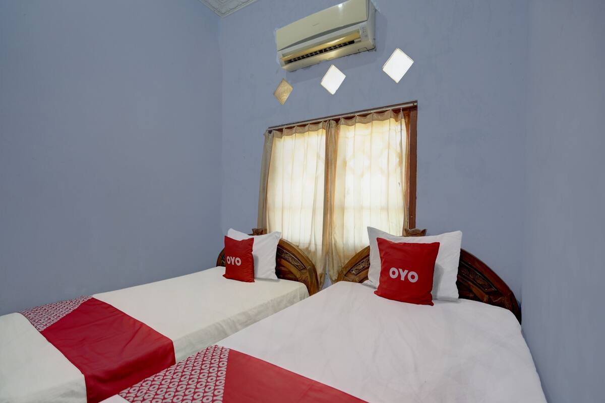 Une chambre d’hôtel avec deux lits, chacun recouvert d’une courtepointe rouge et blanche, et agrémentée d’oreillers assortis. Un appareil de climatisation est fixé au mur au-dessus des lits.