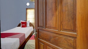 Une pièce avec une armoire en bois, un lit recouvert d’une couvre-lit à motifs rouges et blancs, et une fenêtre avec des rideaux.