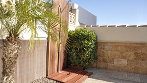 A patio area with a wooden deck, a palm tree, and a hedge. - Luxe 6P Kindervriendelijke Villa met Zwembad, Airco, Internet Wifi, Alarm en BBQ (Mazarrón)