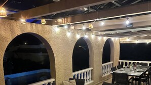 An outdoor dining area with tables and chairs, arched windows, and string lights. - Luxe 6P Kindervriendelijke Villa met Zwembad, Airco, Internet Wifi, Alarm en BBQ (Mazarrón)