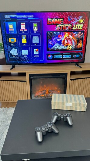 Televisiossa näkyy videopeli, takan edessä on kaksi peliohjainta pöydällä.