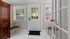 A hallway with a white door, two windows, a wooden bench, and a cabinet.