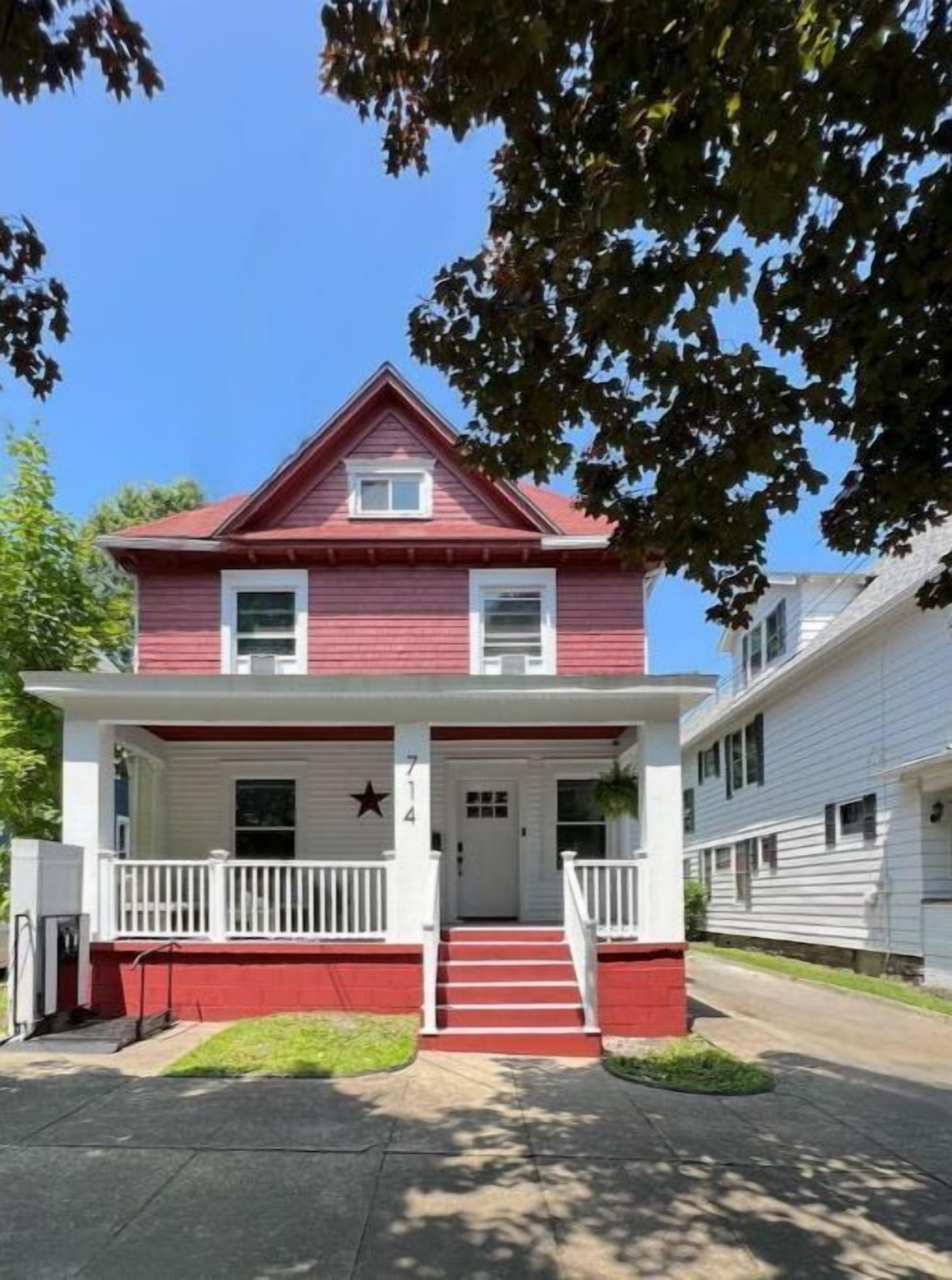 Une maison à deux étages, à la façade rouge et blanche, avec un porche à l’avant doté de balustrades blanches et une décoration en forme d’étoile au-dessus de la porte.