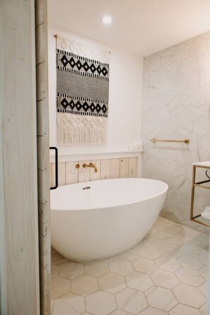 A modern bathroom with a freestanding bathtub, wooden paneling, and a patterned towel hanging on the wall. - Studio 3 at Beer Ranch Project. Walk to Wimberley Square. Unwind. Stay awhile. (Wimberley)