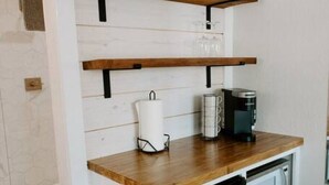 Una cuina petita amb prestatges de fusta, una cafetera i un rellotge.