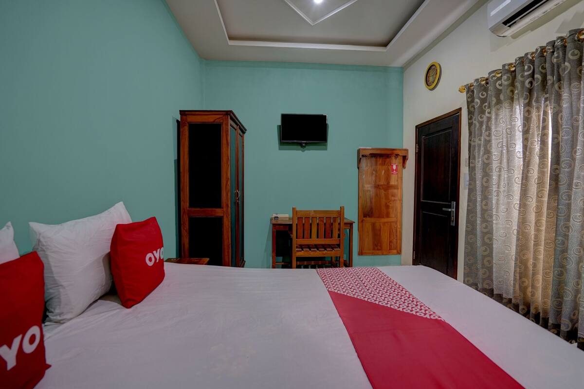 Een slaapkamer met een bed, een houten garderobe, een televisie aan de muur en een deur met gordijnen.