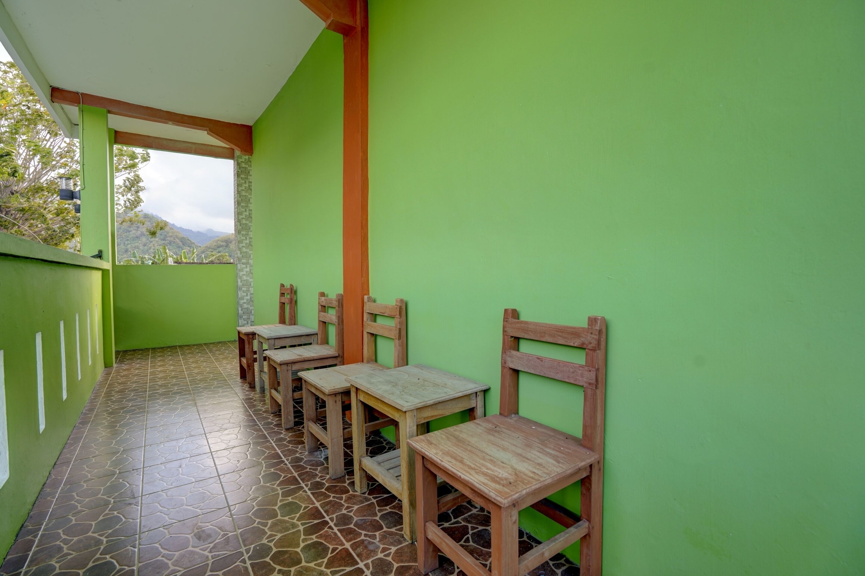 Un espace extérieur aménagé, abrité et doté de tables et de chaises en bois, de murs recouverts de verdure et d’un sol carrelé.