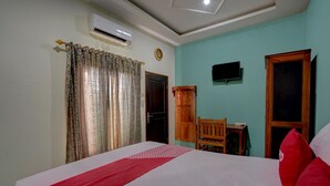 Habitación de hotel con cama, una silla de madera, una mesita pequeña, aire acondicionado y televisor.