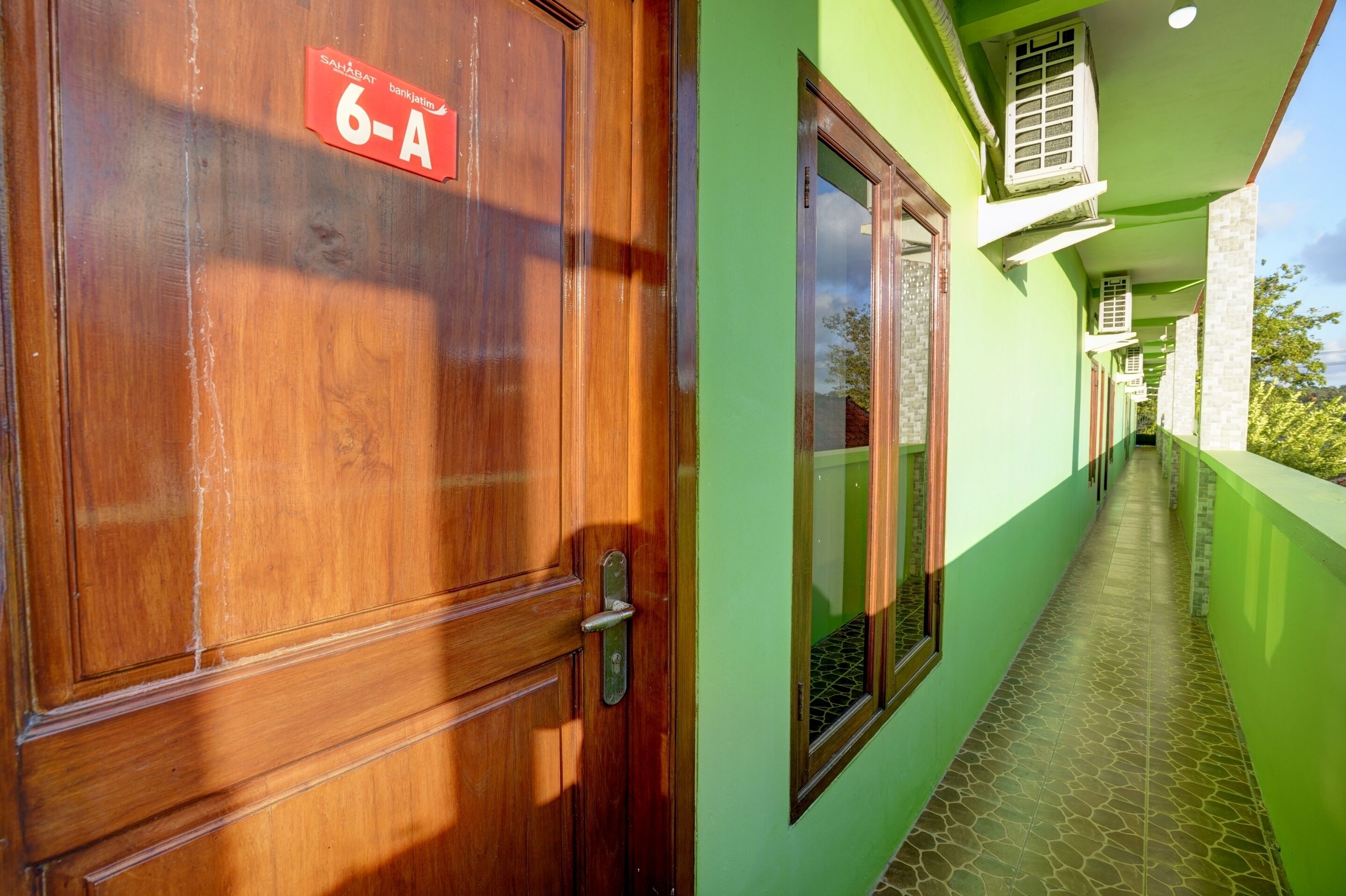 A hallway with a wooden door labeled "6-A" and a green wall with a tiled floor.