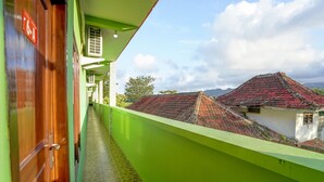 Un estrecho pasillo con pared verde y suelo de baldosas, que conduce a un balcón con vistas a casas tradicionales de tejados rojos.