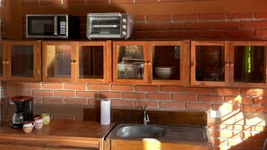 Een keuken met een bakstenen muur, houten kasten, een magnetron, een broodrooster, een koffiezetapparaat en een gasfles.