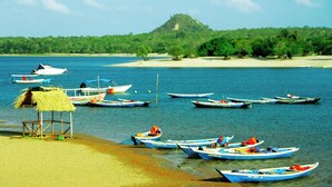 Une plage où sont amarrés plusieurs petits bateaux près du rivage, une cabane à toit de chaume et, au loin, une colline.