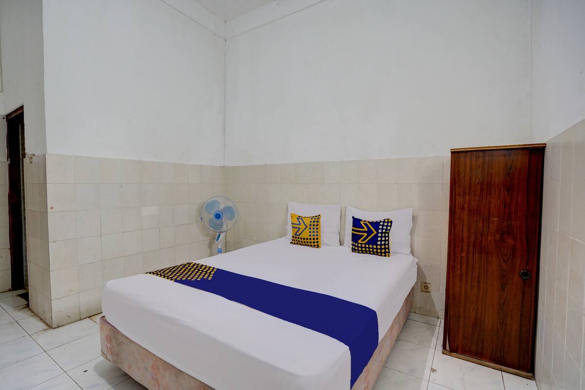Un dormitorio con cama, una puerta de madera y un ventilador.