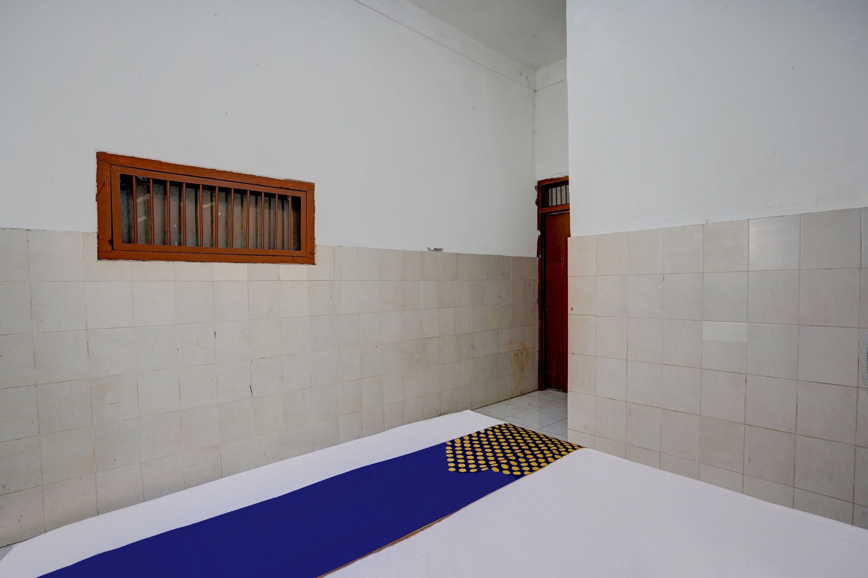 A small, narrow room with white tiled walls, a wooden door, and a window with a wooden frame.