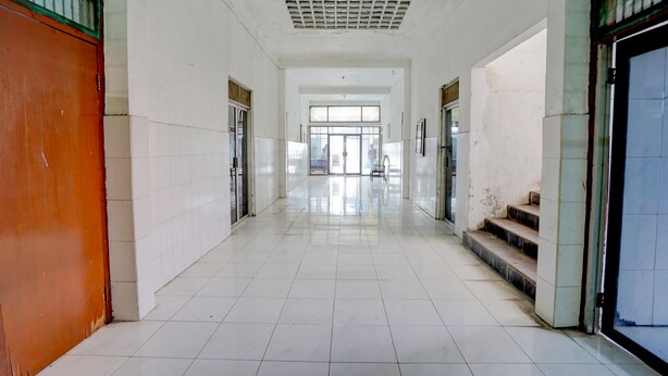 Un pasillo con pisos de baldosas blancas y puertas, que conduce a una habitación luminosa con ventanas amplias.