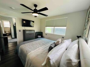 Cozy bedroom with a single bed, ceiling fan, flat-screen TV, and window with blinds.