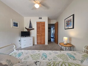 A bedroom with a bed, a TV on a dresser, a wooden door, and a hallway leading to another room. - Fenimore Mill 1C - Pool and Beautiful Gulf Views! (Cedar Key)