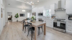 Une cuisine moderne avec des meubles blancs, une grande table à manger et un four en acier inoxydable.