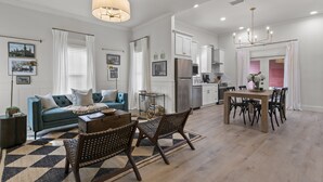 Un grand espace de vie comprenant un canapé, une table basse et une table à manger avec des chaises. Il y a également un coin cuisine équipé d’un réfrigérateur et de placards.