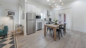 Une cuisine moderne avec des meubles blancs, des appareils en acier inoxydable et un coin repas comprenant une table et des chaises en bois.