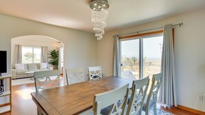 Un comedor con mesa de madera y sillas blancas, un candelabro y vistas a través de amplios ventanales.