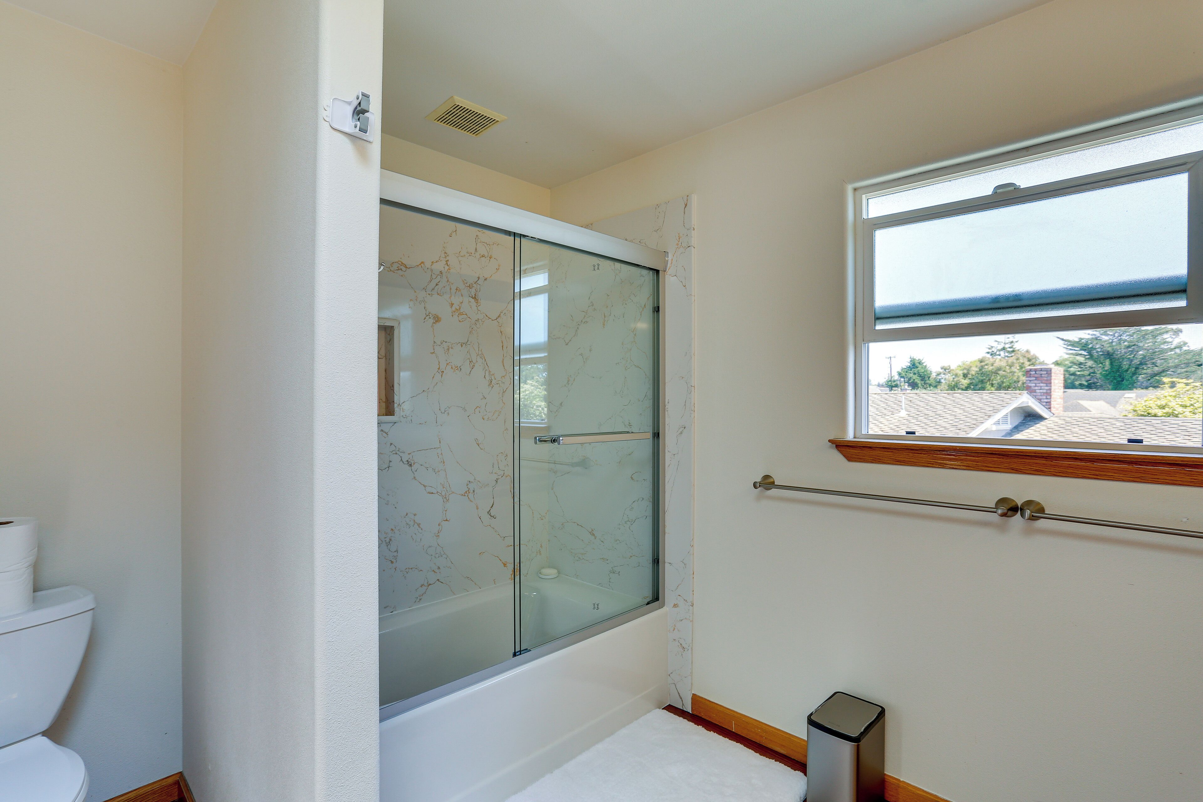 Een badkamer met een douche met glazen wand, een toilet en een raam met uitzicht.
