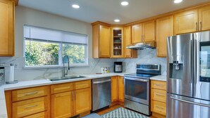 Una cocina moderna con armarios de madera, electrodomésticos de acero inoxidable, horno empotrado y una ventana con persianas.