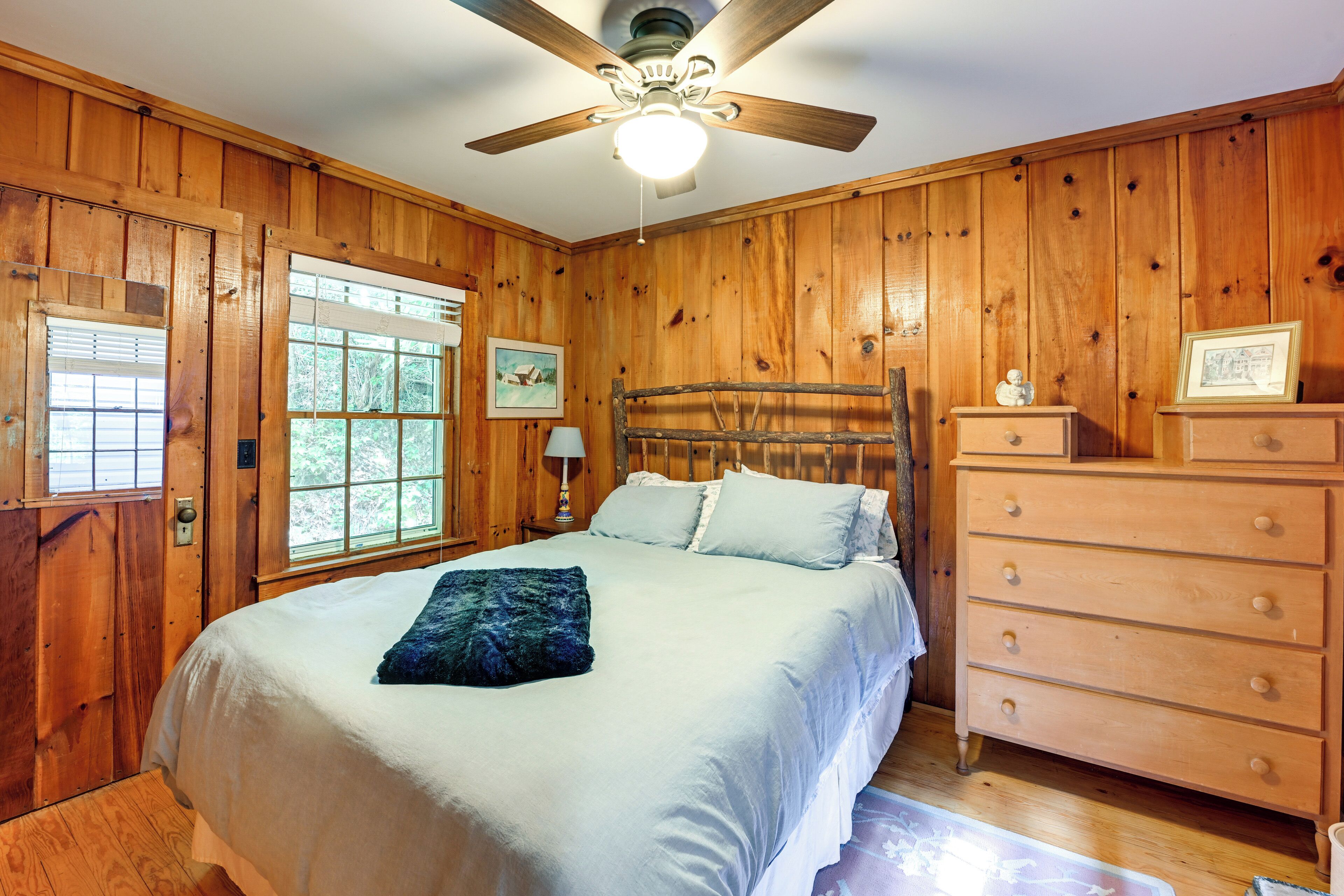 A wooden-paneled bedroom with a bed, a dresser, and a ceiling fan.