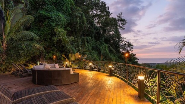 A wooden deck with lounge chairs and a sofa, surrounded by lush greenery and a railing with lights. - Villa Fortuna Best Piece of Heaven in Costa Rica (Provincia de Puntarenas)