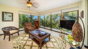 A spacious living room with a large window, a ceiling fan, a flat-screen TV, and a coffee table. - Villa Fortuna Best Piece of Heaven in Costa Rica (Provincia de Puntarenas)