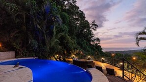 A swimming pool with a curved edge, surrounded by lush greenery and a wooden deck with outdoor seating. - Villa Fortuna Best Piece of Heaven in Costa Rica (Provincia de Puntarenas)