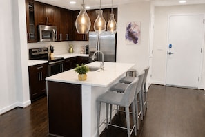 A modern kitchen with dark wood cabinets, stainless steel appliances, a white island with bar stools, and pendant lighting. - The Luxe | City View | Romantic Escape (Atlanta)