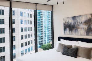 A modern hotel room with a large bed, a view of a high-rise building, and a painting on the wall. - The Luxe | City View | Romantic Escape (Atlanta)